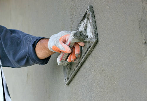 Man's hand plastering a wall with trowel. Selective focus.